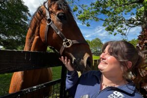 A woman stands smiling at a horse.