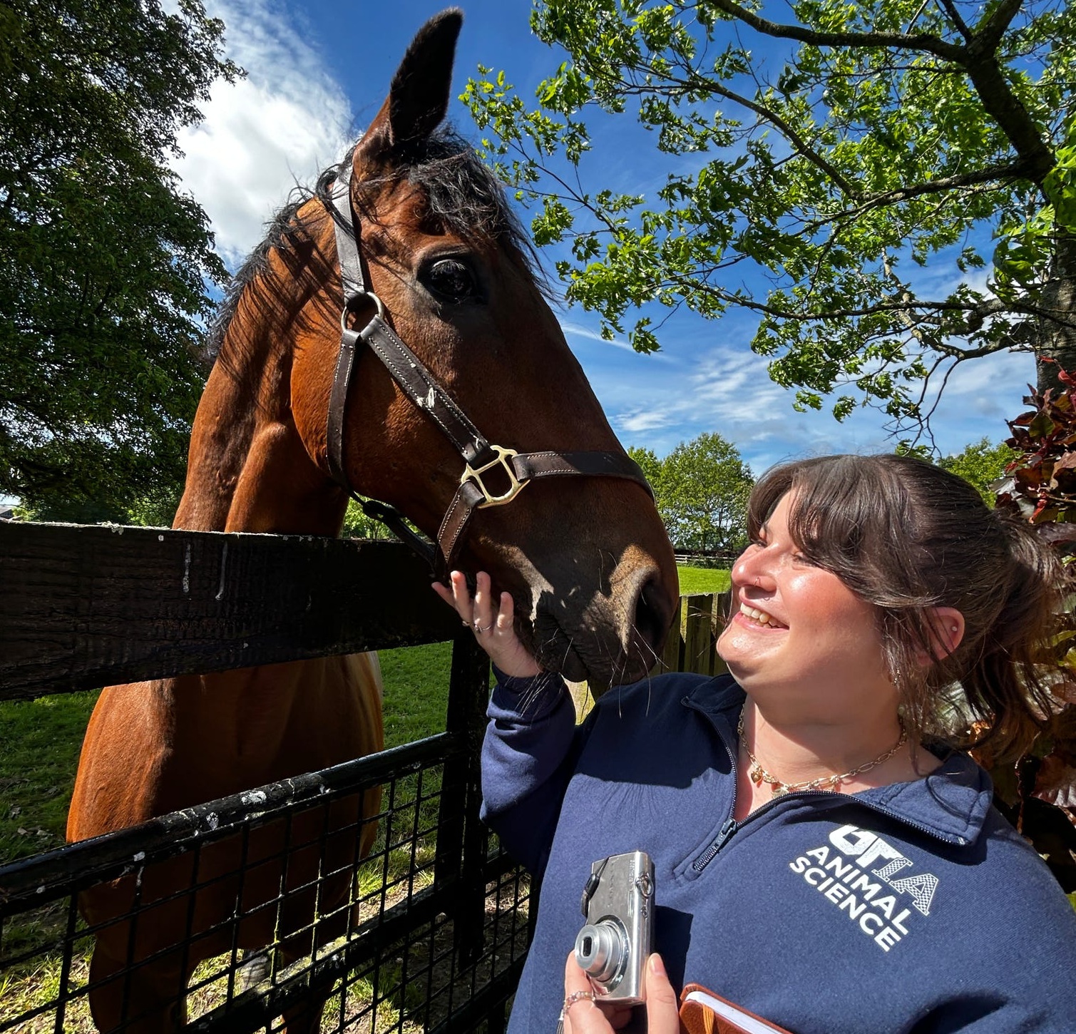 A woman stands smiling at a horse.